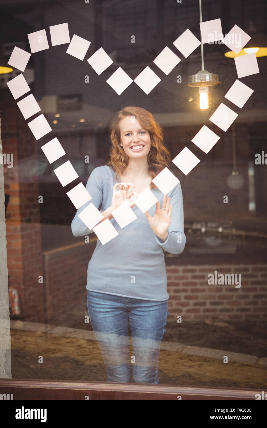 Portrait of happy woman sticking adhesive notes in heart shape Stock Photo