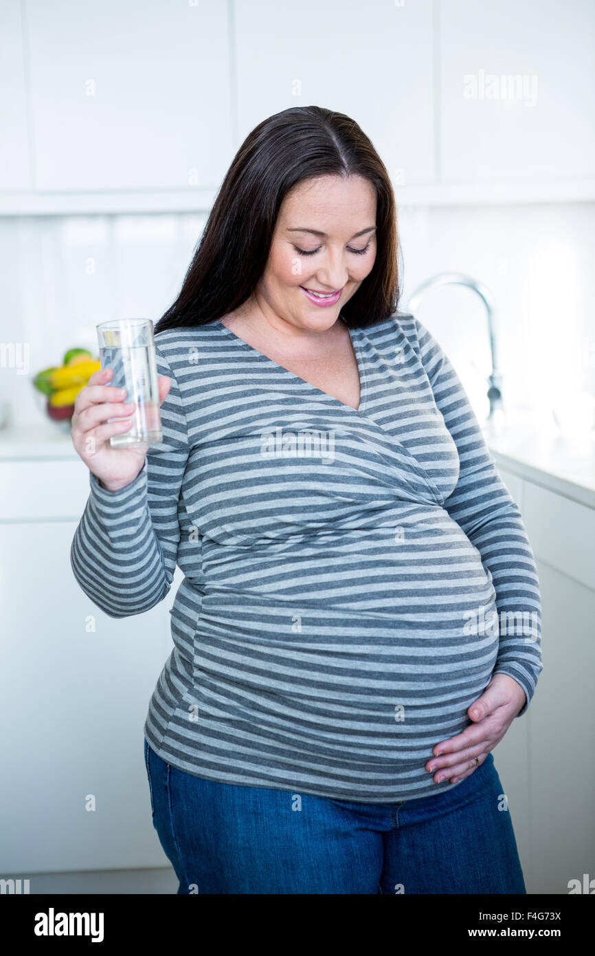 Beautiful pregnant woman touching her belly drinking a glass of water Stock Photo