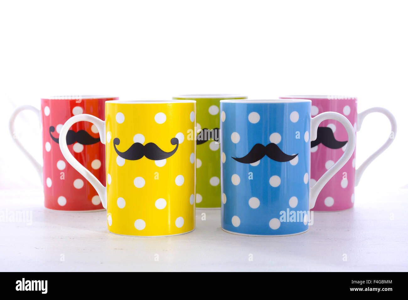 Colorful polka dot coffee mugs with mustaches for November Mens health awareness on white wood table. Stock Photo