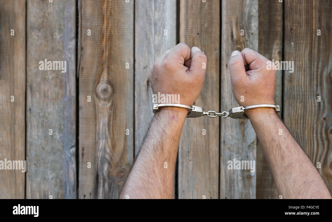 Arrest, closeup shot man's hands with handcuffs in front of plank wood