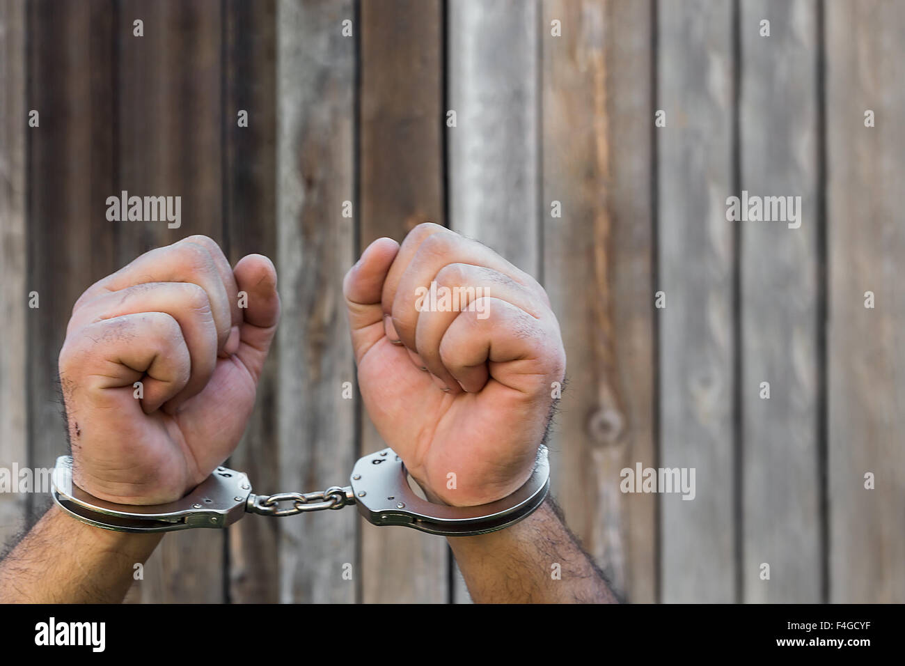 Arrest, closeup shot man's hands with handcuffs in front of plank wood