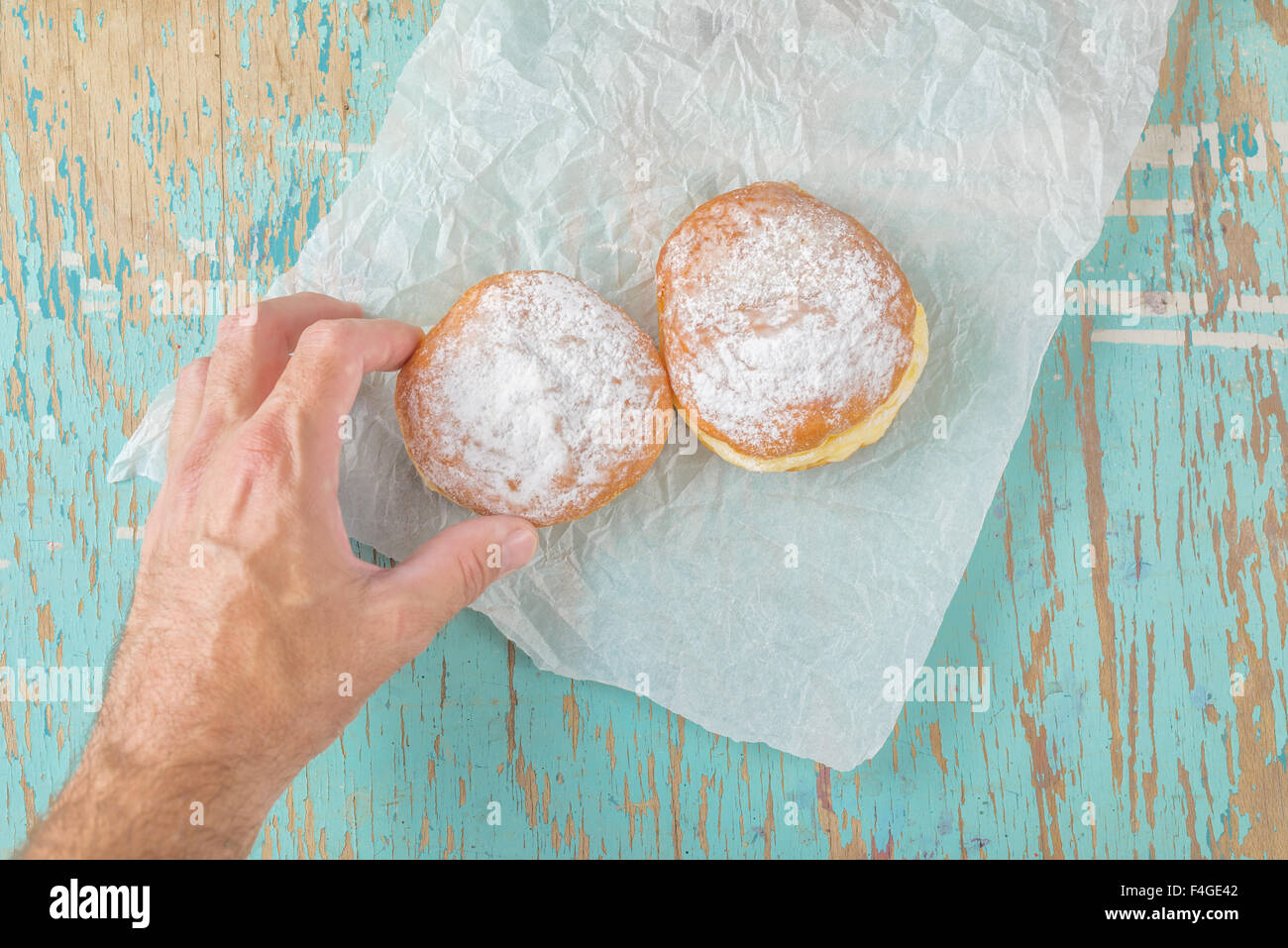 Male hand reaches and picking sweet sugary donut from rustic wooden kitchen table, classic hannukah sufganiyot or tasty bakery d Stock Photo