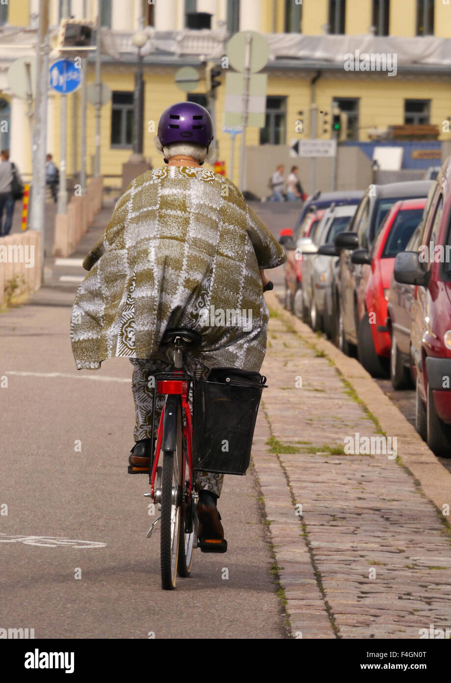 An eccentric looking woman on a bicycle wearing a purple cycling helmet and a shawl Stock Photo