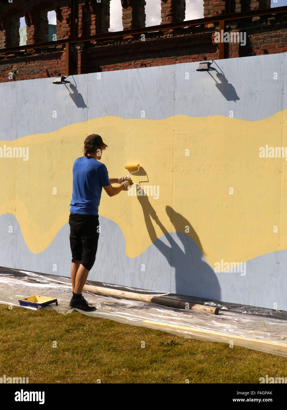 A man paining a hoarding outside with a paint roller on a sunny day Stock Photo