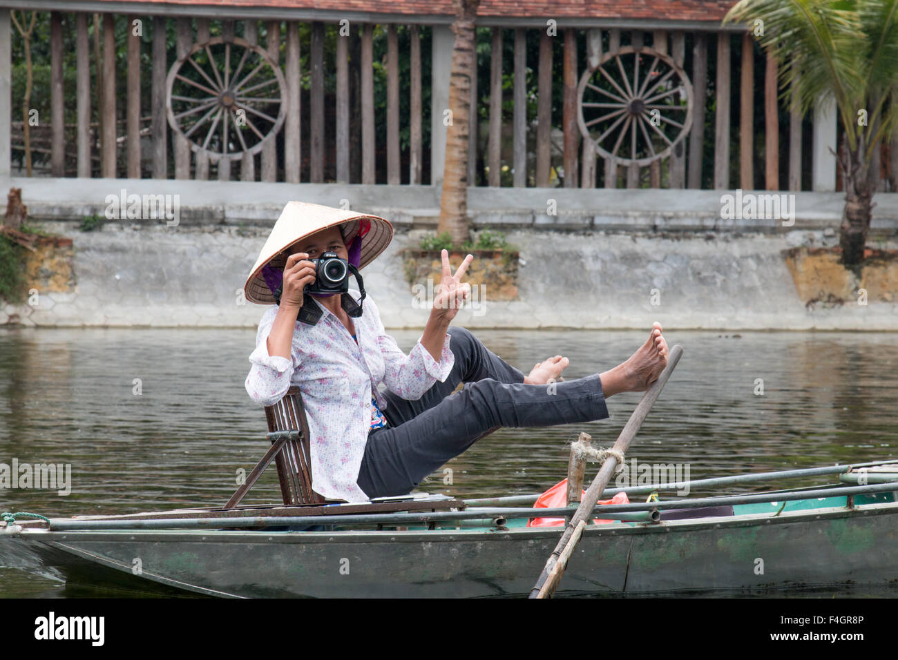 vietnamese photographer taking tourists shots poses with a V for vietnam sign, ngo dong river,Tam Coc,Vietnam Stock Photo