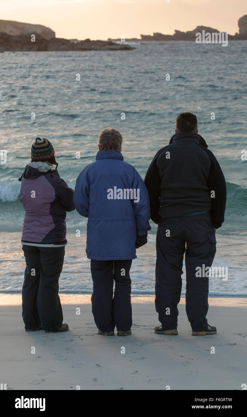 Three people looking out to sea waiting for the sunset Stock Photo