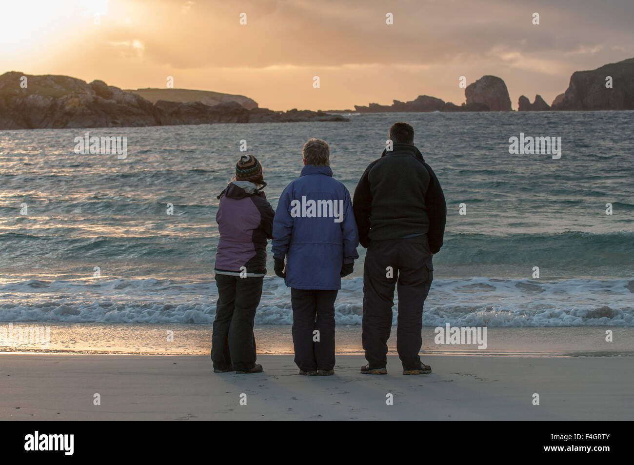 Three people looking out to sea waiting for the sunset Stock Photo