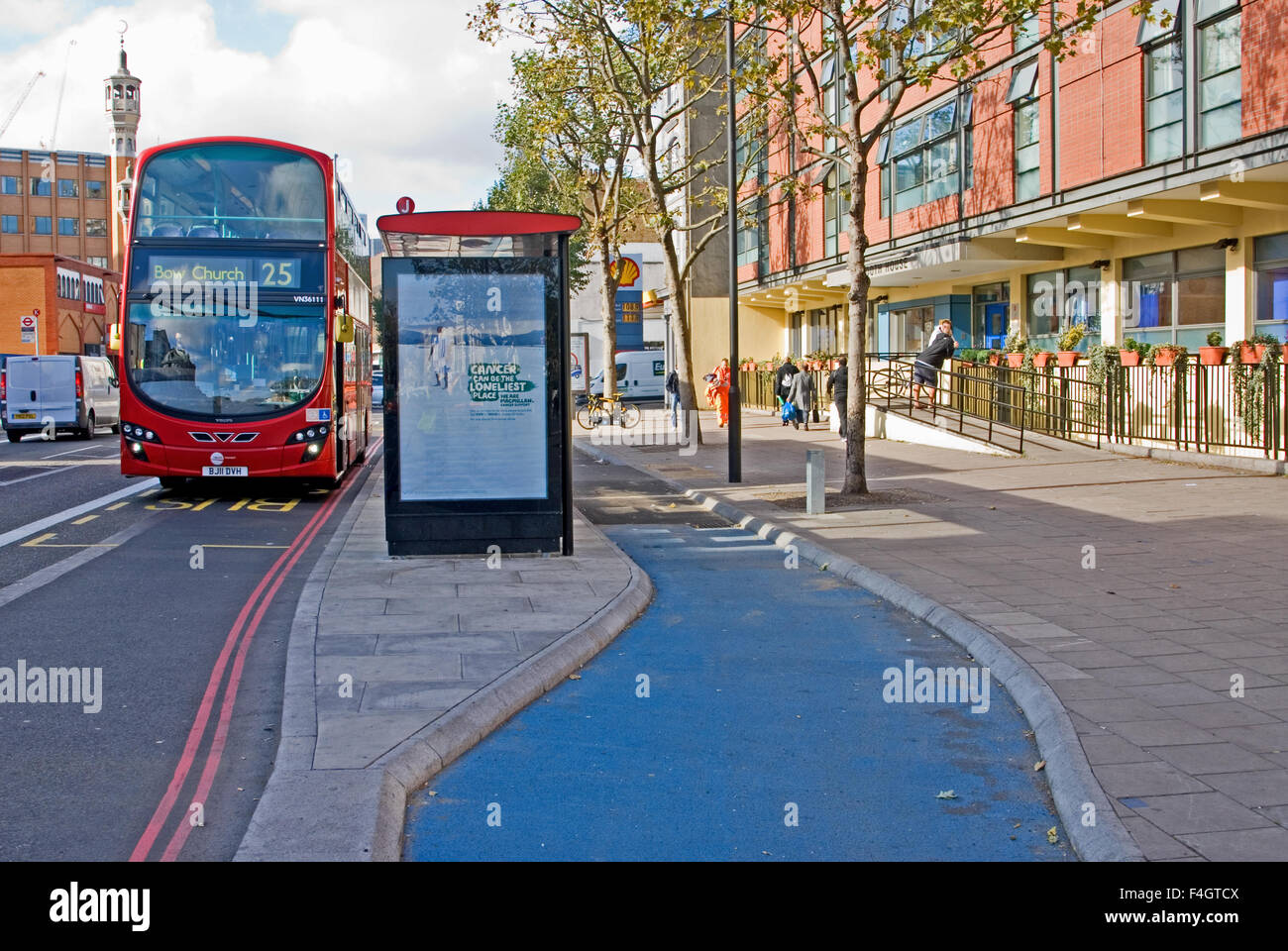 A red modern double deck London bus passes a bus stop with a new cycle track bypass in Whitechapel, East London. Investment in bicycle infrastructure. Stock Photo