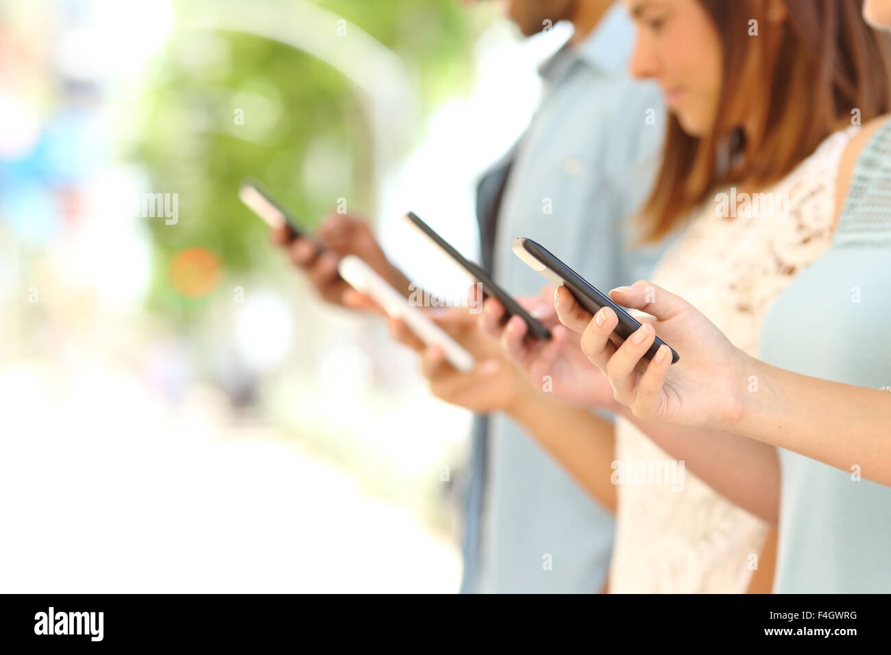 Four friend hands texting in their smart phones in the street with a blurred background Stock Photo
