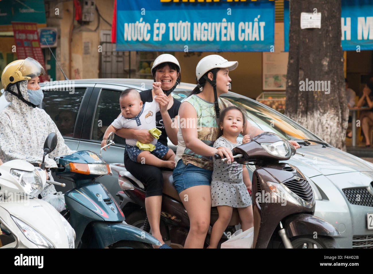 two mothers and two children on the same scooter motorbike riding through Hanoi city centre, the capital city of Vietnam. Stock Photo