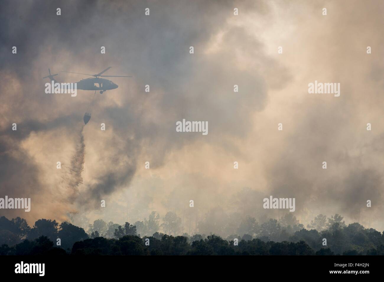 A Texas Army National Guard UH-60 Black Hawk helicopter drops water on the Hidden Pines Fire October 17, 2015 near Bastrop, Texas. Stock Photo