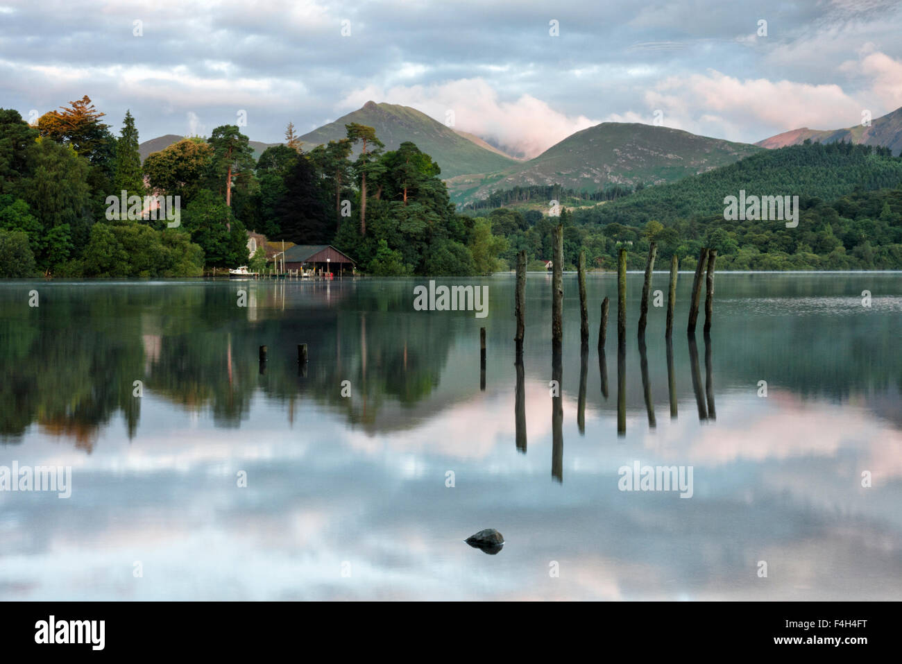 Remains of an old jetty with the fells and a boathouse at dawn reflected on Derwent Water in the Lake District National Park, Keswick, Cumbria Stock Photo