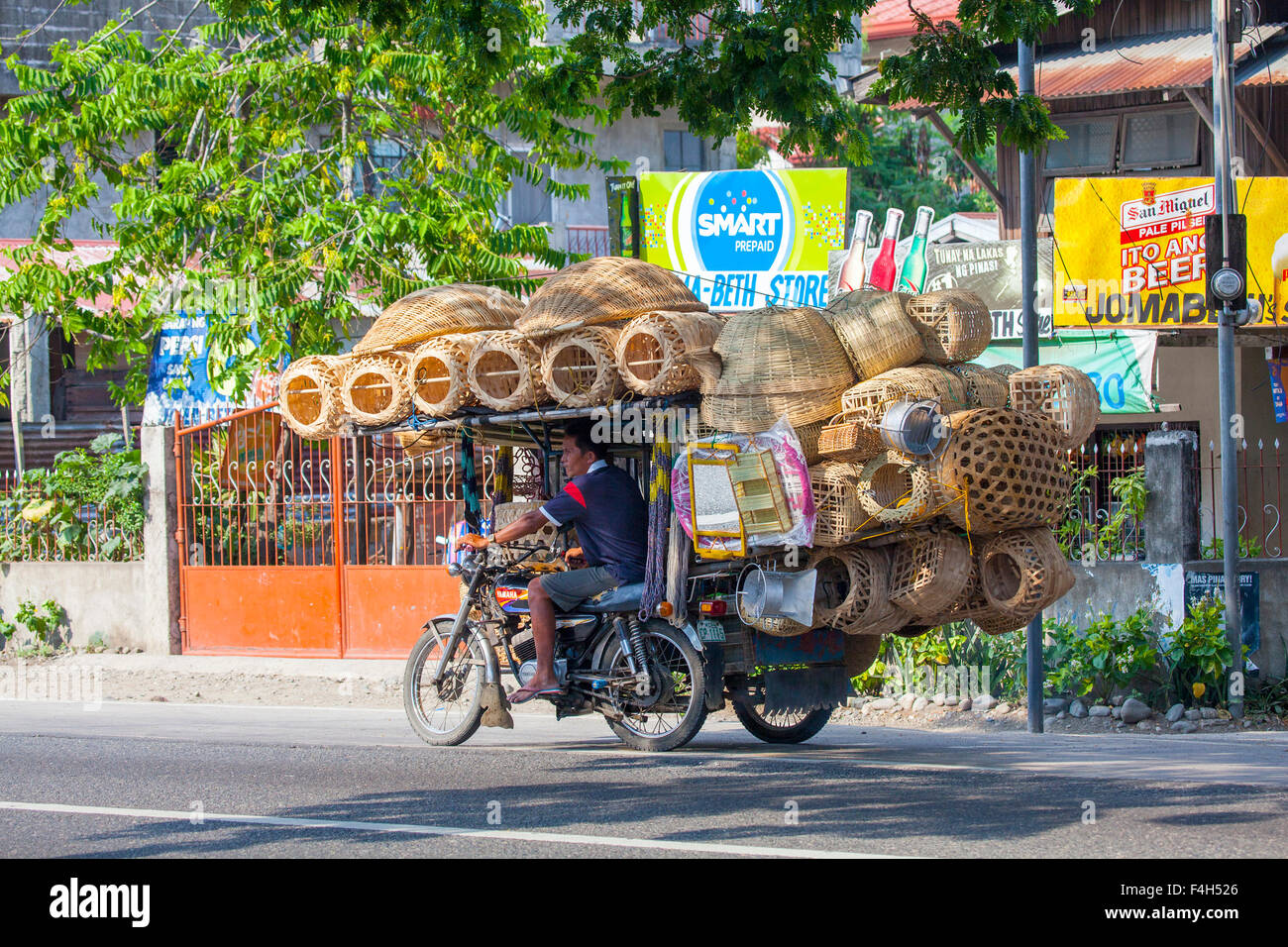 A Filipino man drives his motorcycle which is heavily overloaded with woven rattan baskets that he sells along city roadsides. Stock Photo