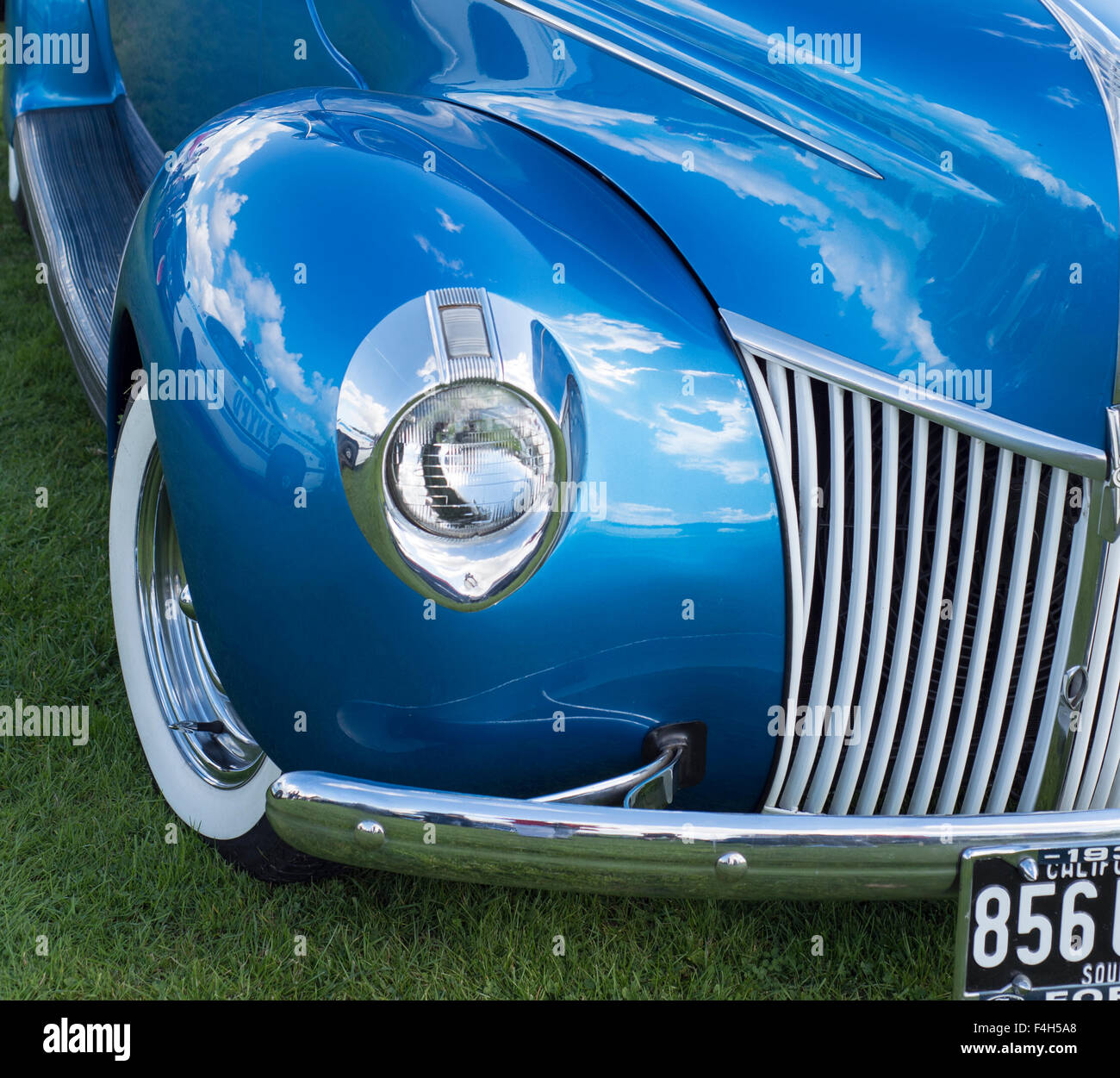 Blue car, headlamp, glass, reflector, circle, silver, grille, white walled tires, reflection of sky, cloud reflection, grass, Stock Photo