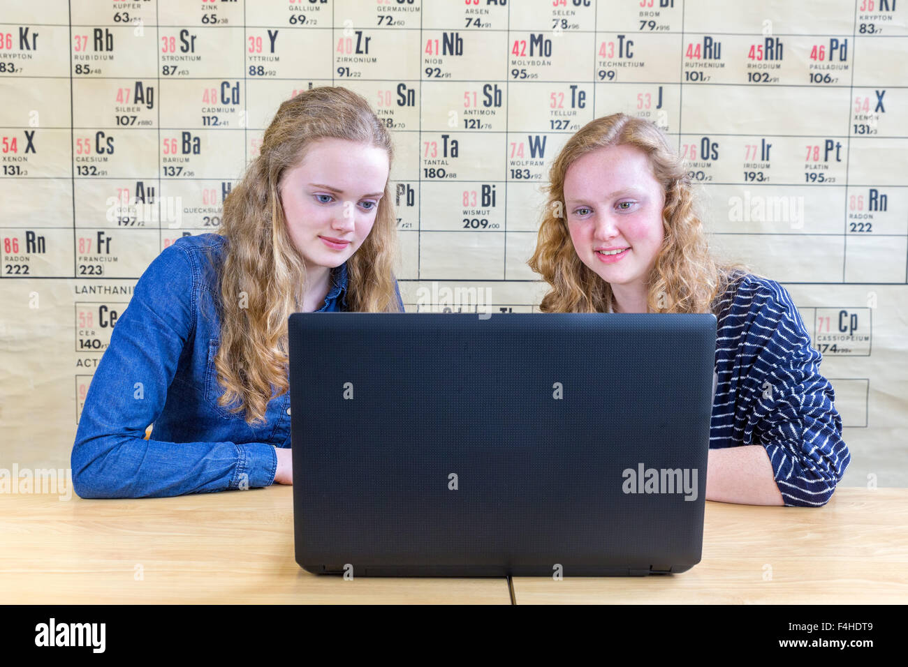 Two caucasian teenage girls looking at laptop in chemistry class in front of wallchart showing periodic table Stock Photo