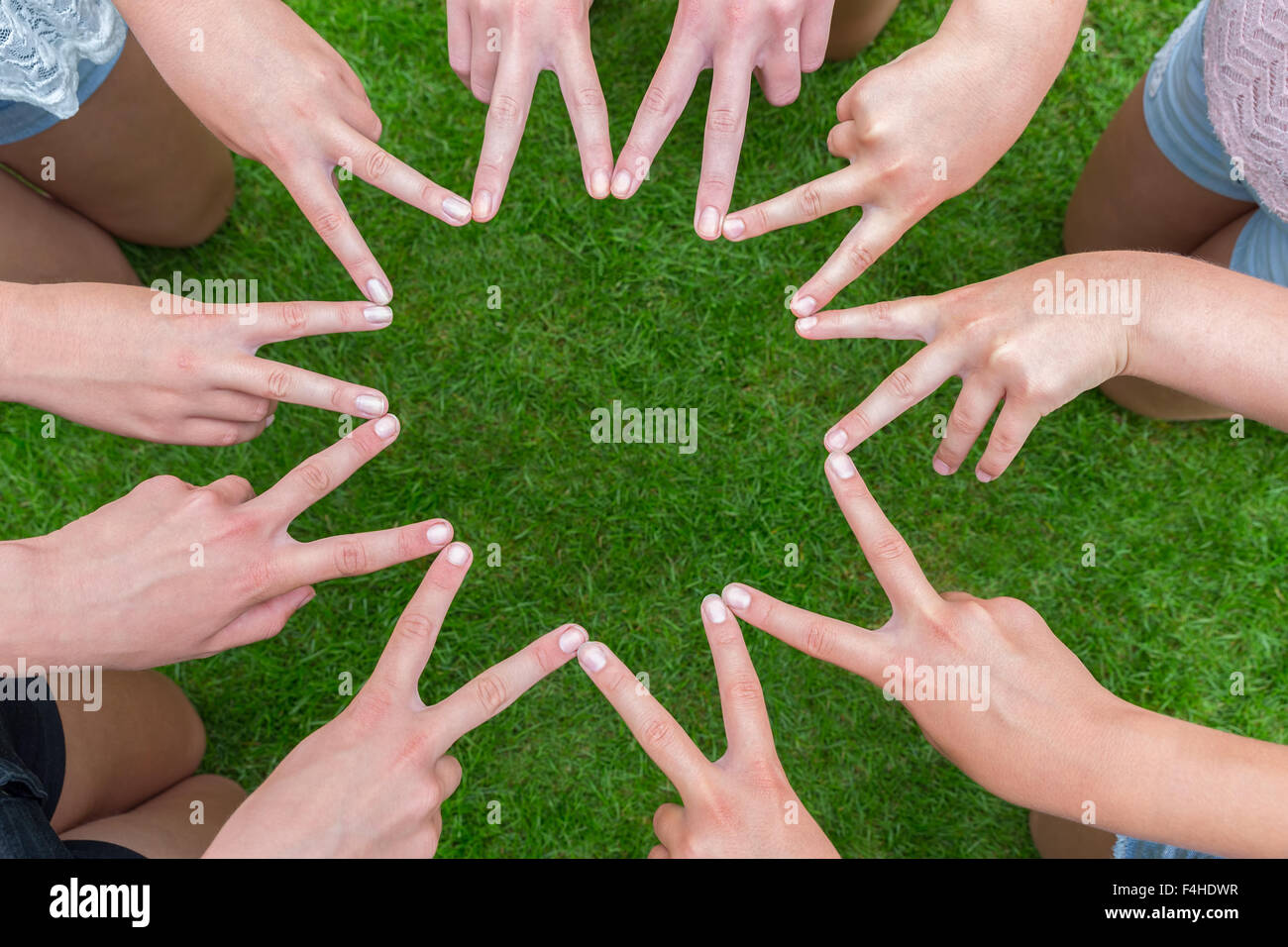 Many arms of girls with hands making ten pointed star above green grass Stock Photo