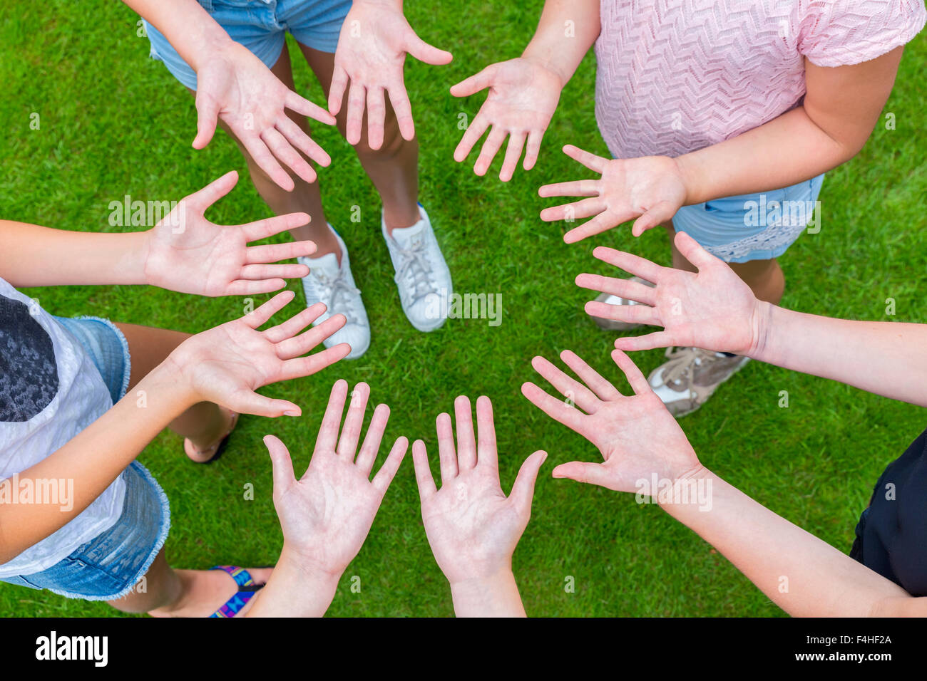 Ten arms of children in circle with palms of hands up above green grass Stock Photo