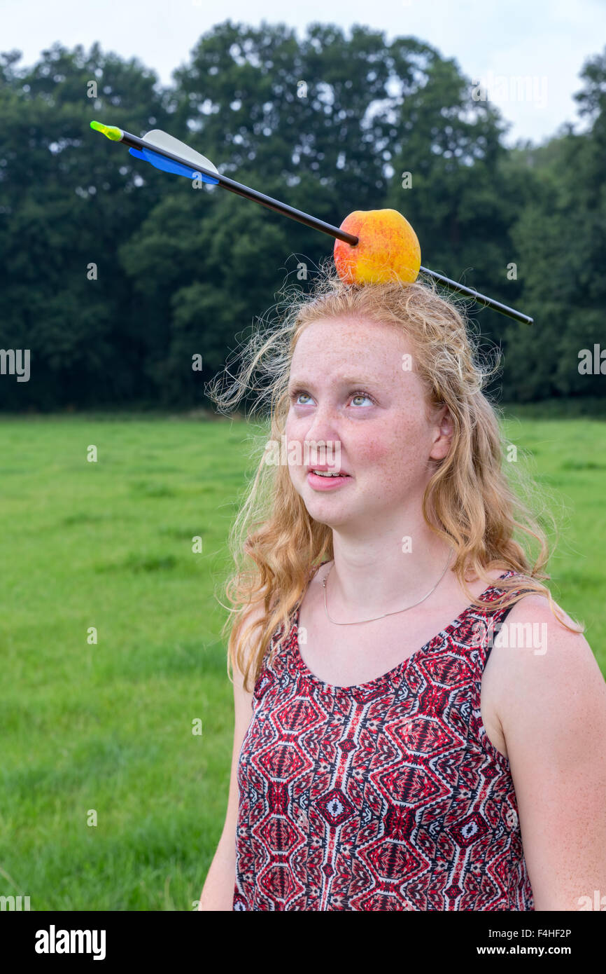 Young woman looking afraid at arrow in apple on head outdoors Stock Photo