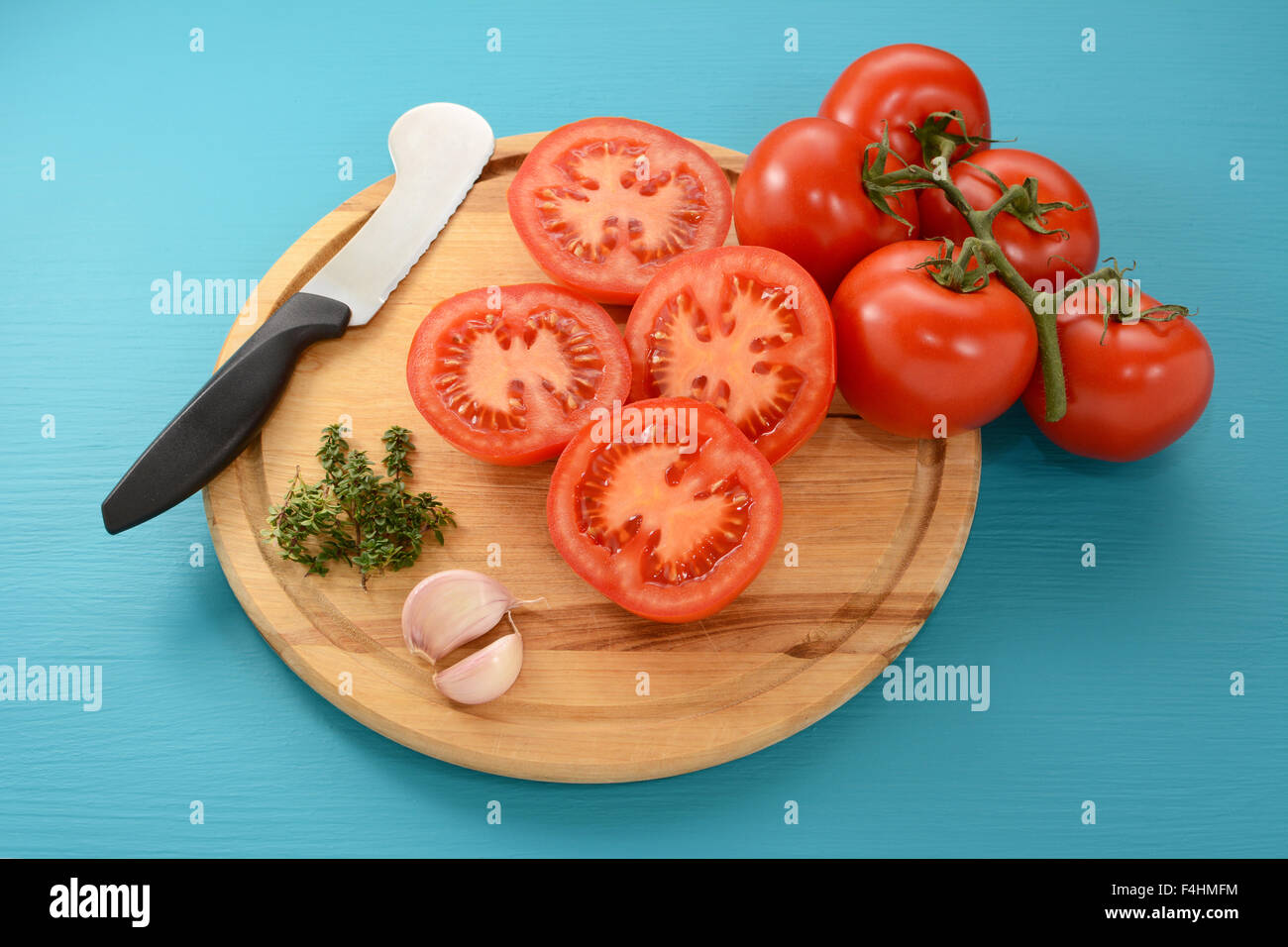 Sliced and whole tomatoes with garlic and thyme, ready for oven roasting, with a tomato knife Stock Photo