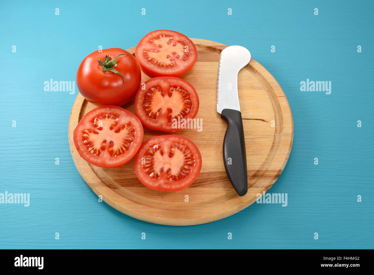 Whole tomato and four cut halves with a tomato knife on a wooden cutting board Stock Photo