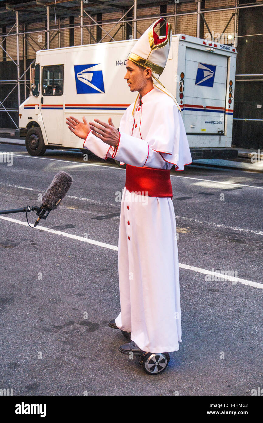 young actor in Pope costume spreads hands in benediction before rolling away down Manhattan street on space board popemobile Stock Photo