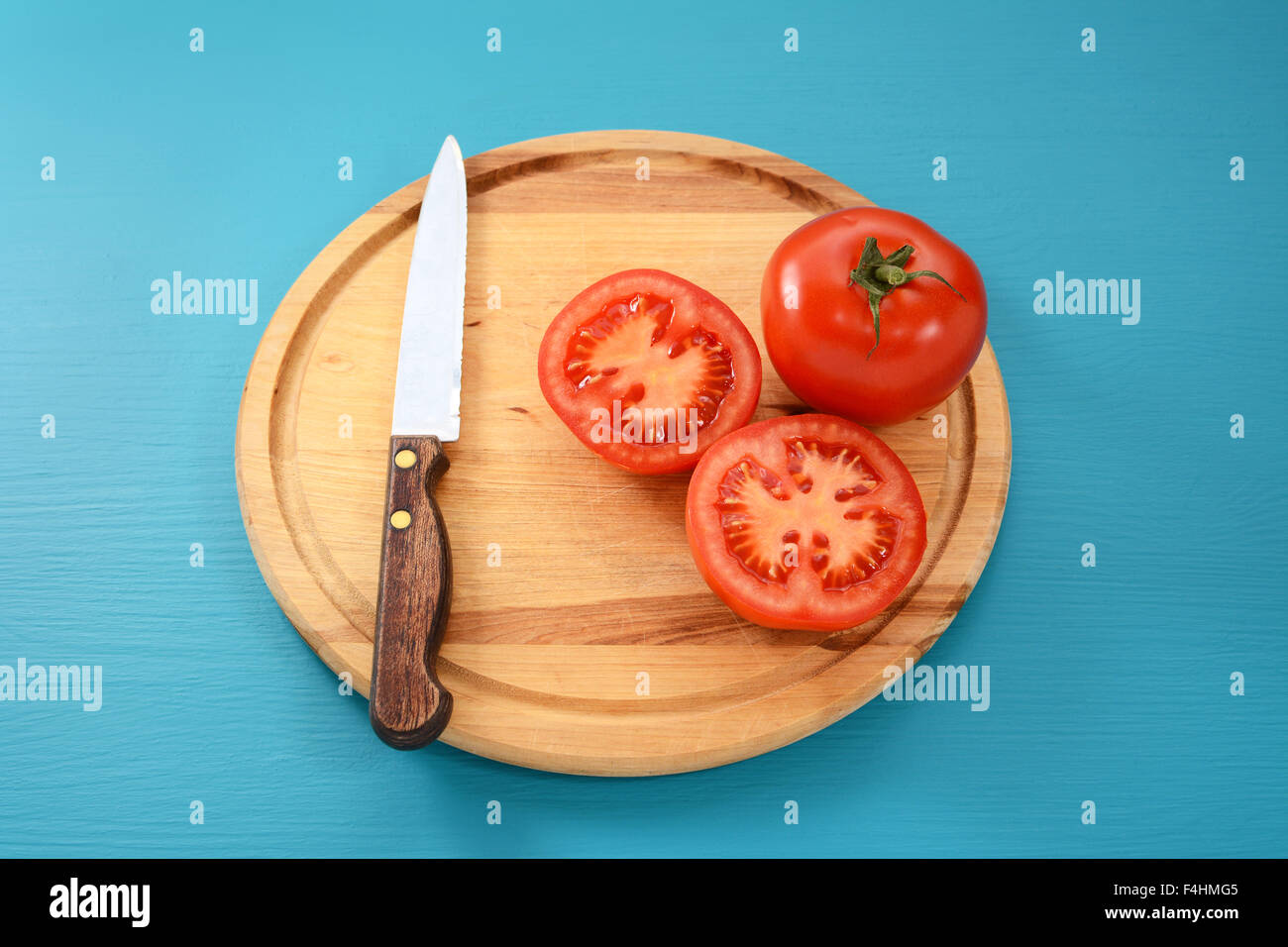 Whole and halved red tomato with serrated kitchen knife on a wooden chopping board Stock Photo