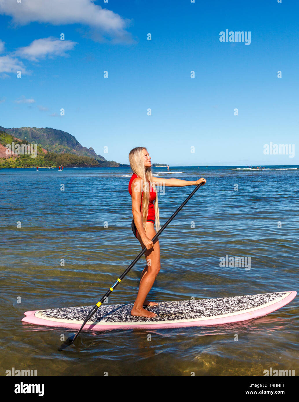 Woman stand up paddling in Hanalei Bay, with Mt. Makana, called Bali Hai, in distance Stock Photo