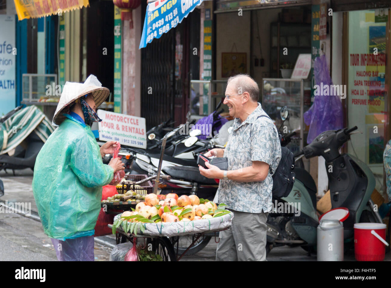 western tourist visitor buying fruit from a vietnamese lady with bicycle in Hanoi old quarter,Capital city,Vietnam Stock Photo