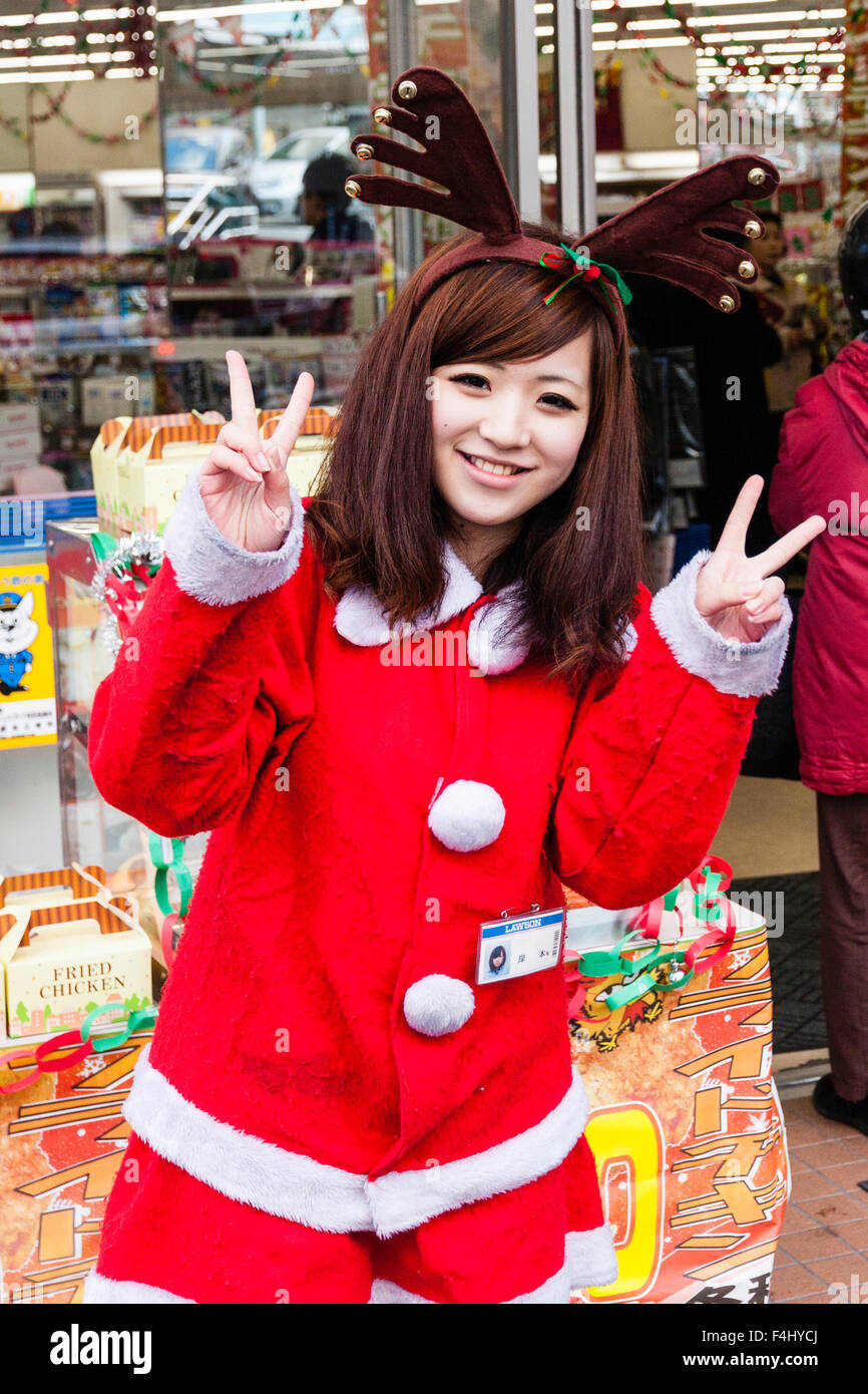 Japan, Wakayama. Teenage Japanese women dressed as Santa Claus, standing posing for viewer. Smiling with both hands raised in peace gesture. Stock Photo