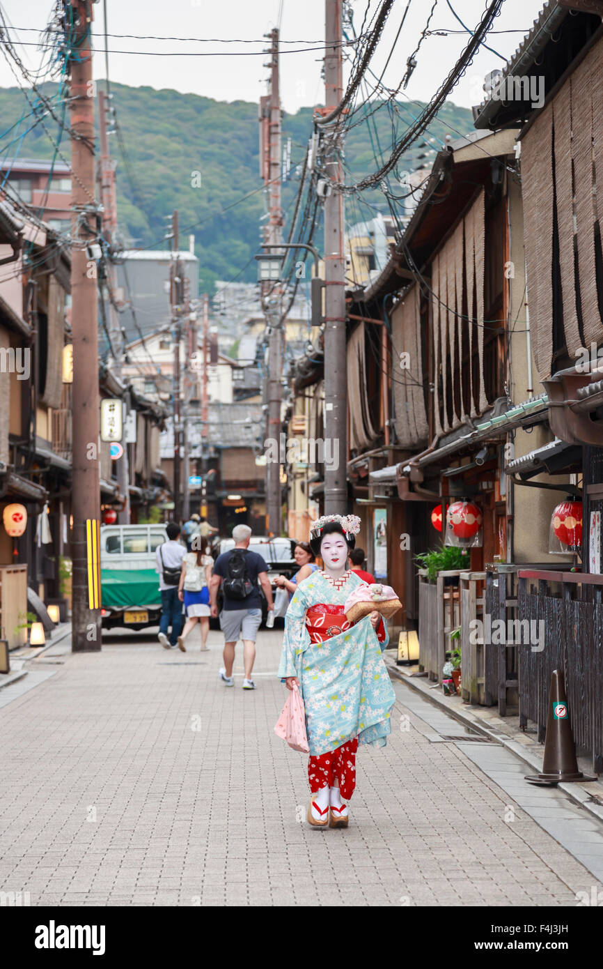 Maiko, apprentice geisha, walks to evening appointment past traditional wooden buildings, Gion, Kyoto, Japan, Asia Stock Photo