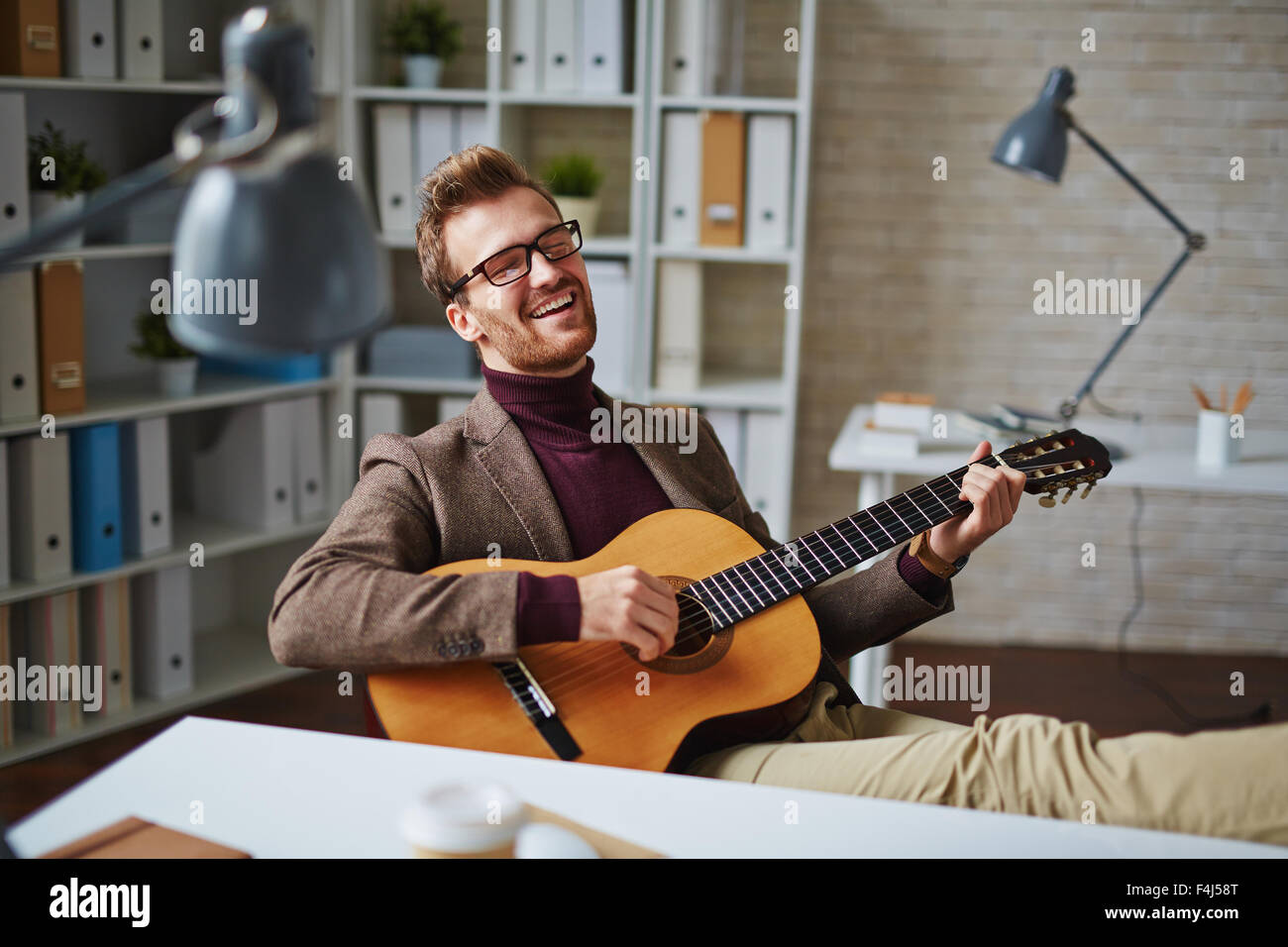 Young man playing guitar at office hires stock photography and images