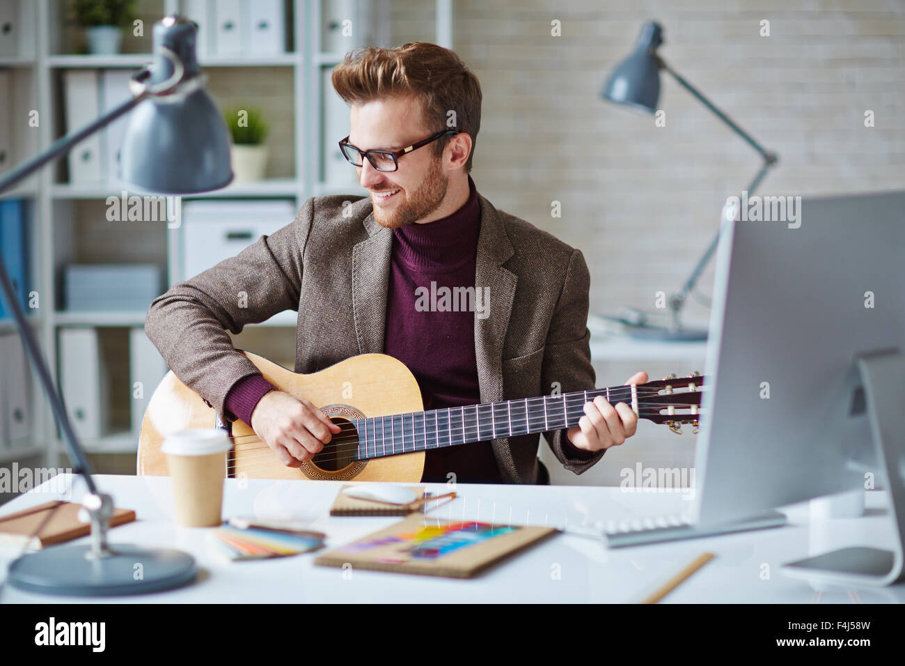 Modern young businessman playing the guitar at workplace Stock Photo