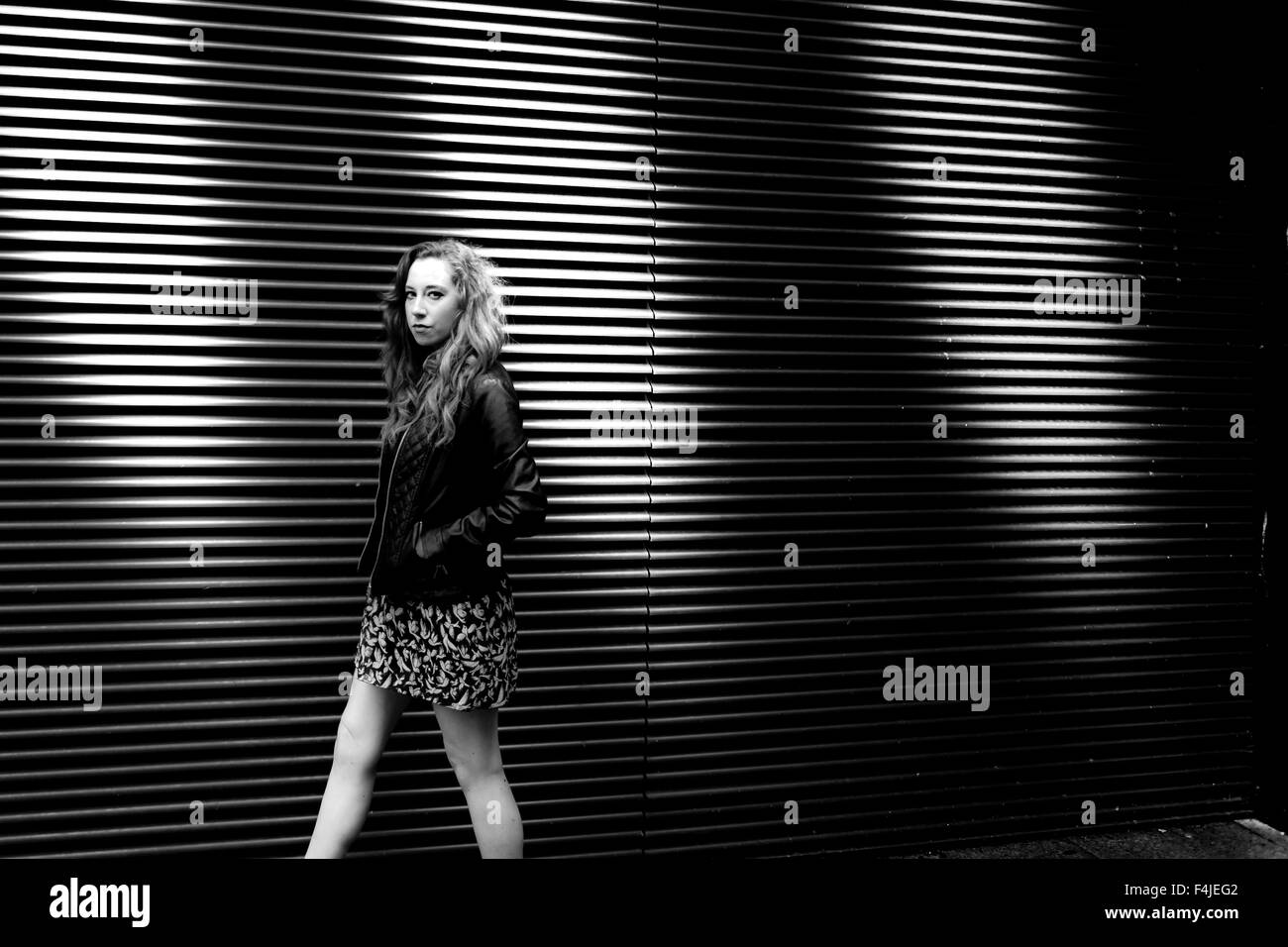 Girl walking alongside a louvered wall looking towards the camera Stock Photo