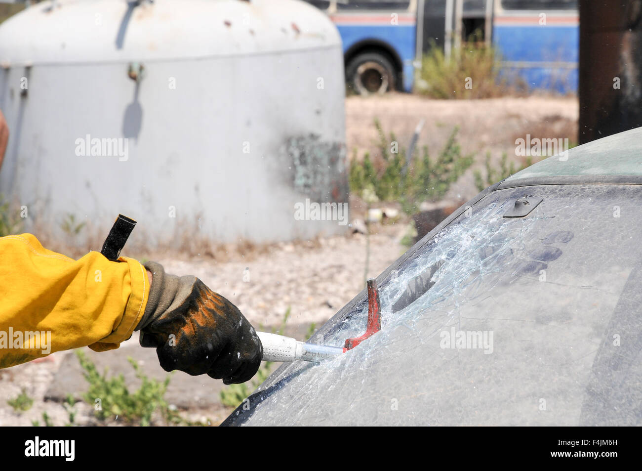 Firefighter uses an axe to break the front windshield of a car to rescue the trapped driver and passengers Stock Photo