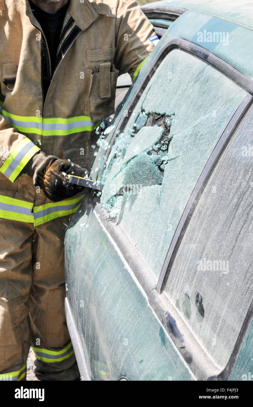 Firefighter uses an axe to break a car's side window to rescue the trapped driver and passengers Stock Photo