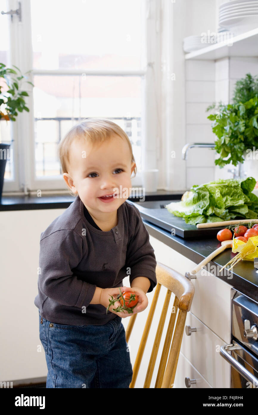 Little boy in kitchen holding cherry tomato Stock Photo - Alamy