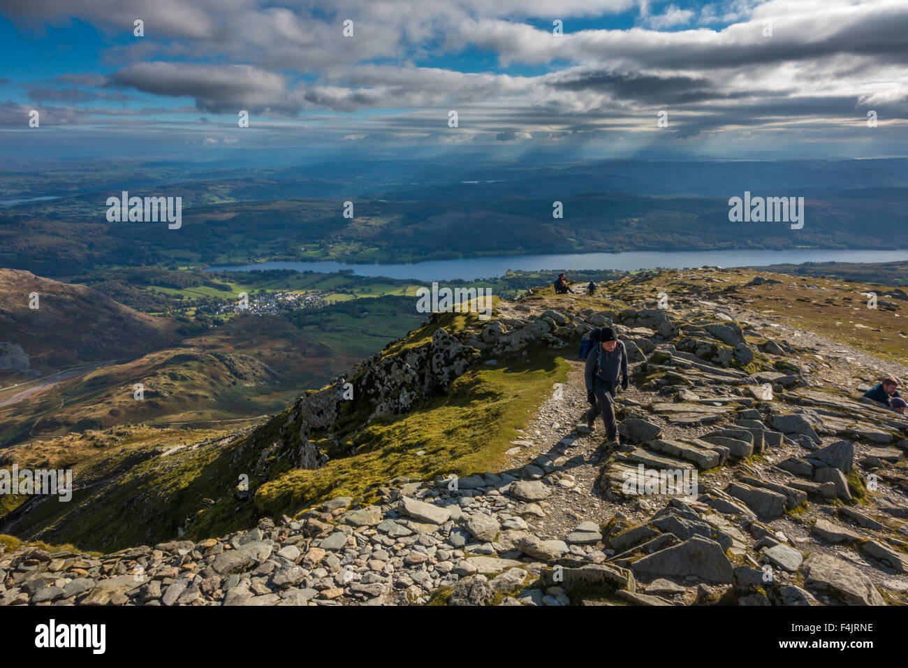 Hikers walking up the last ridge onto the summit of the Old Man of Coniston with views over Coniston Water, Lake District Stock Photo