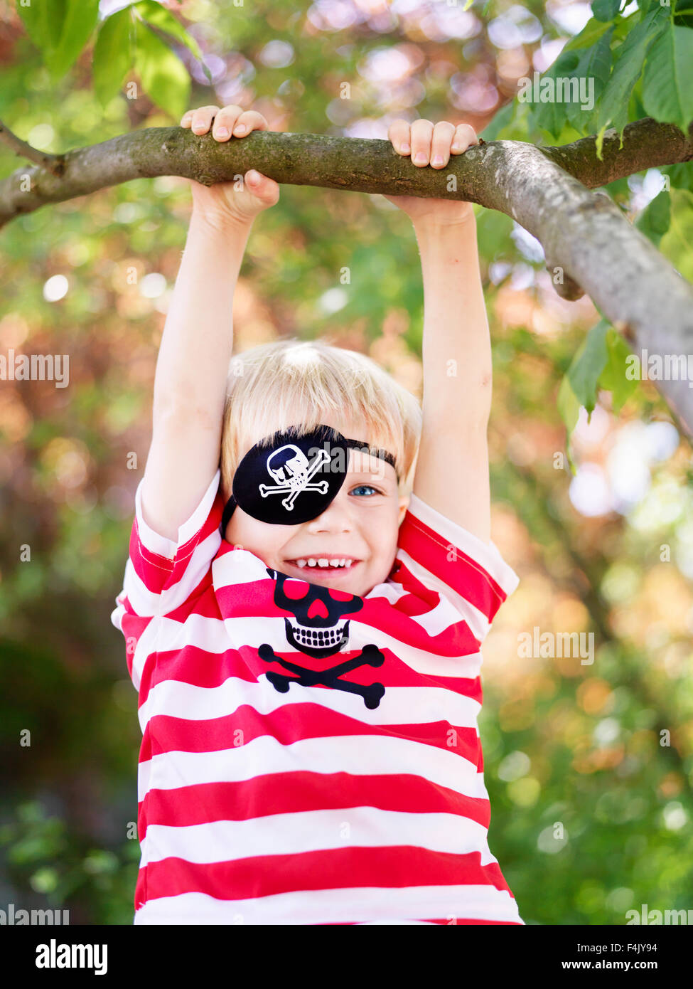 Boy wearing eye patch hanging from branch of tree Stock Photo