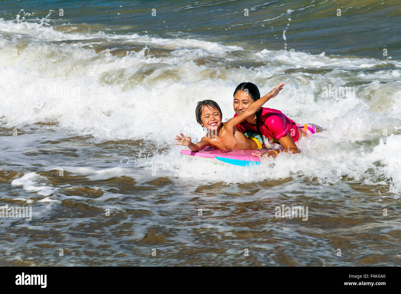 Brother and sister share boogie board at Hanalei Beach on Kauai Stock