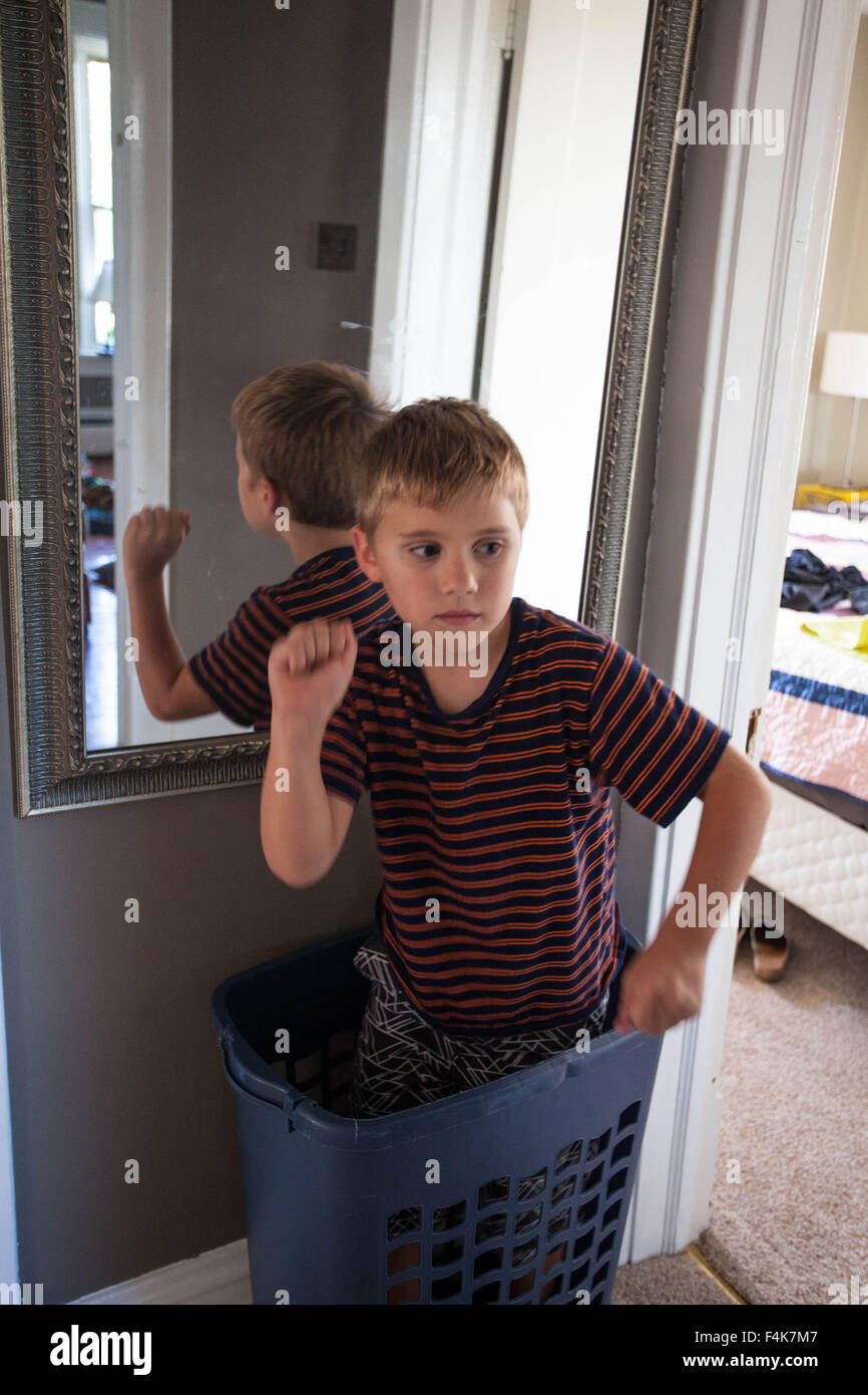 Little Boy plays and stands in a laundry basket in his home hallway Stock Photo