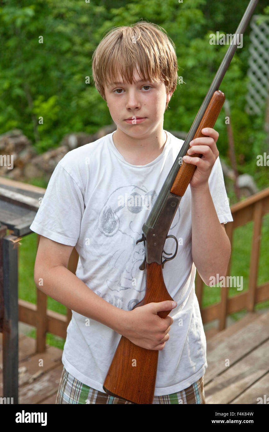Boy age 12 holding shotgun during target practice at family cabin