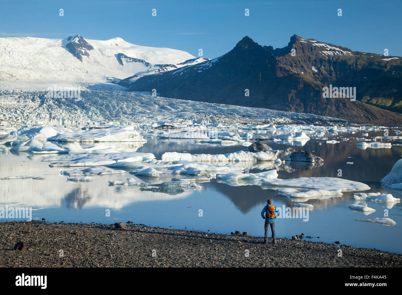 Person beside Fjallsarlon iceberg lagoon, beneath Fjallsjokull glacier. Vatnajokull National Park, Sudhurland, Iceland. Stock Photo