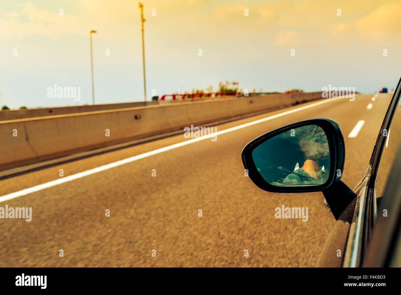 a young man, reflected in the wing mirror, driving a car in a road with several lanes Stock Photo