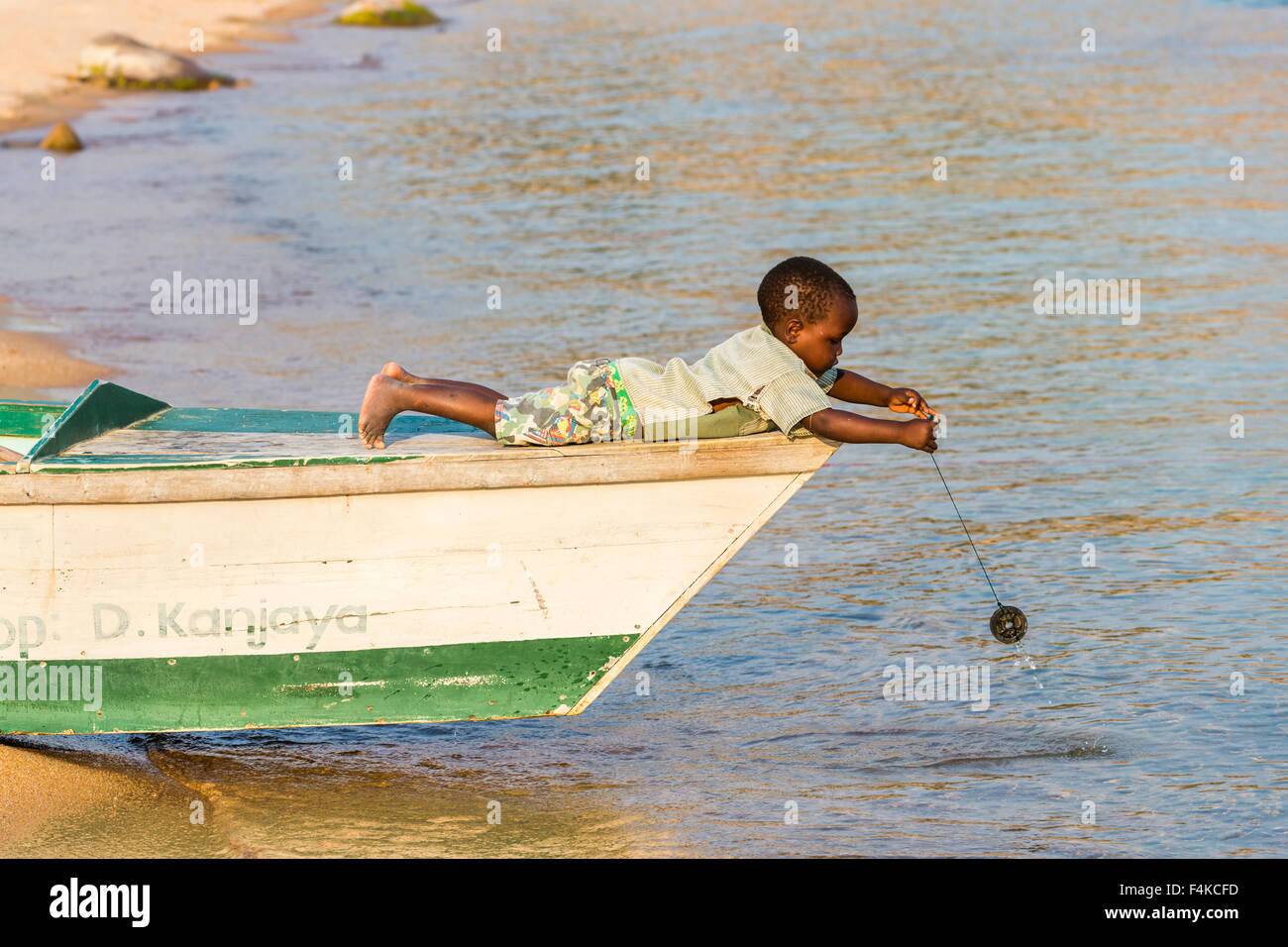 Local young African boy child laying down plays at fishing from a fishing boat, Kaya Mawa, Likoma Island, Lake Malawi, Malawi, south-east Africa Stock Photo