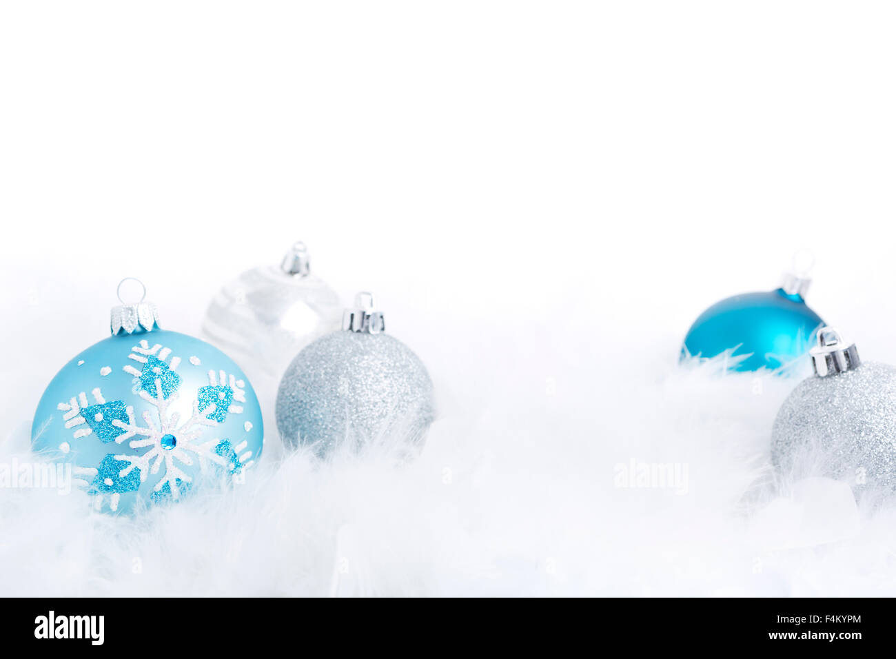 Blue and silver Christmas baubles on a soft feathery surface with a white background. Stock Photo