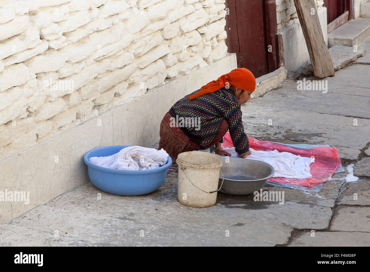 Peasant woman washes clothes in the street of Marpa village, Mustang, Nepal. Stock Photo