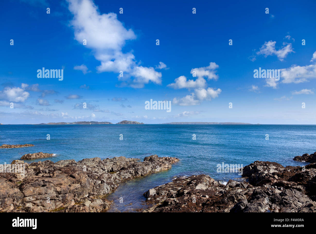 Guernsey rocky coastline, view looking East towards Herm and Sark, bright sun, blue sky Stock Photo