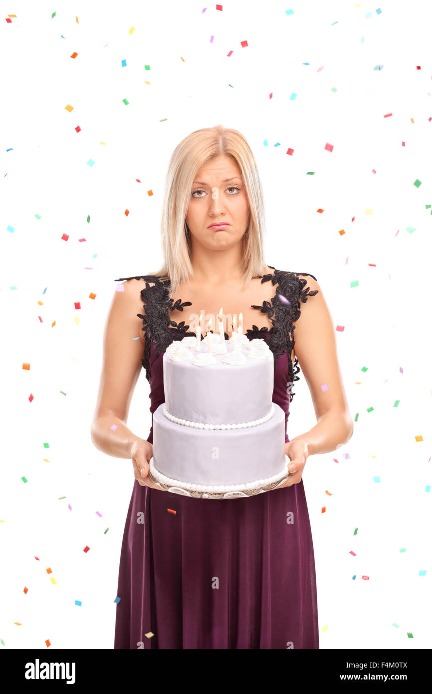 Vertical shot of a sad young woman holding a birthday cake with confetti streamers flying around her Stock Photo