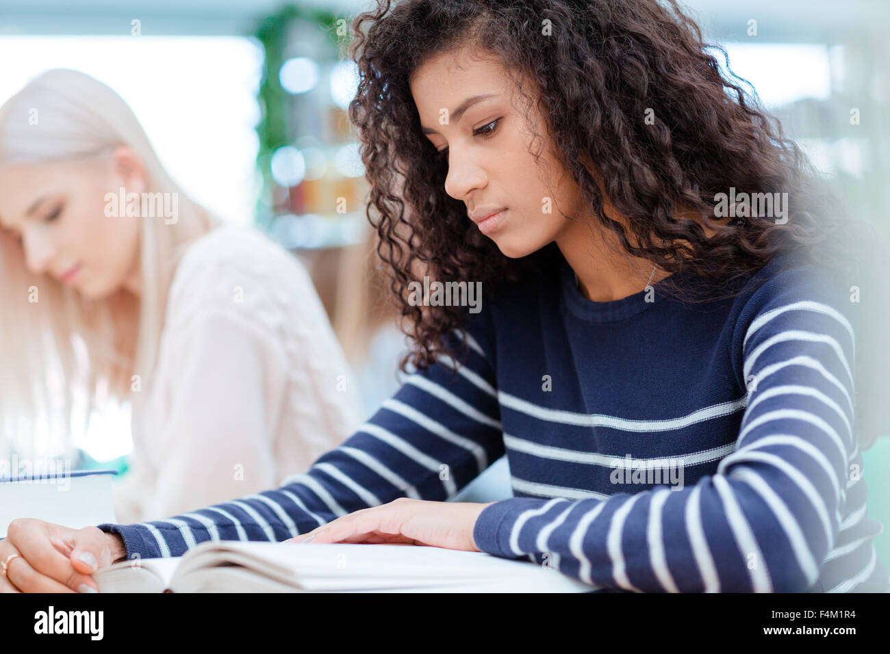 Afro american female student reading book in classroom with classmates on background Stock Photo
