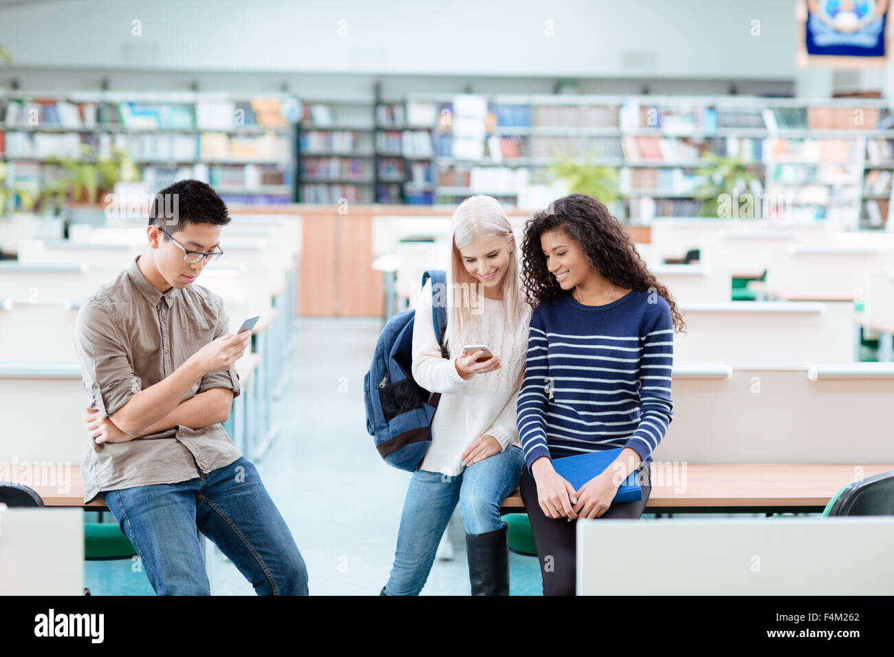Portrait of a happy multi ethnic students using smartphones in the univrsity library Stock Photo